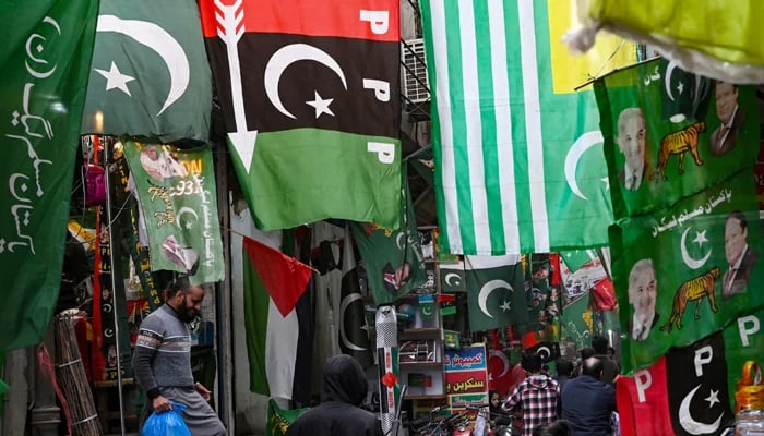 People walk past flags of Pakistan´s political parties displayed for sale at a market in Lahore on January 13, 2024, ahead of the general elections. — AFP