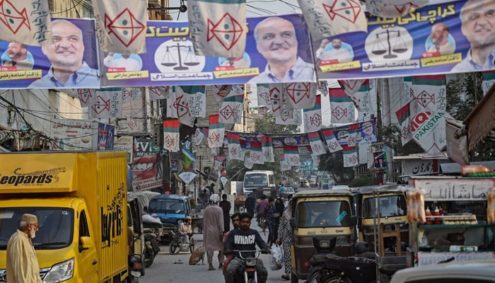 Commuters move past the election banners of Muttahida Qaumi Movement-Pakistan (MQM-P) and Jamaat-e-Islami (JI) parties hung over a street ahead of the upcoming general elections, in Karachi on January 24, 2024. — AFP