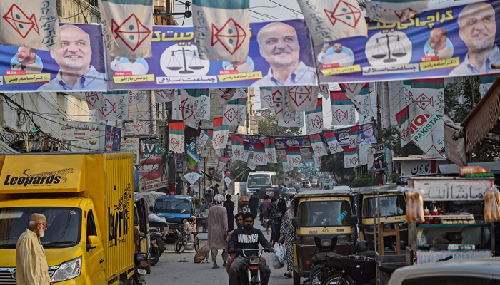 Commuters move past the election banners of Muttahida Qaumi Movement-Pakistan (MQM-P) and Jamaat-e-Islami (JI) parties hung over a street ahead of the upcoming general elections, in Karachi on January 24, 2024. — AFP)