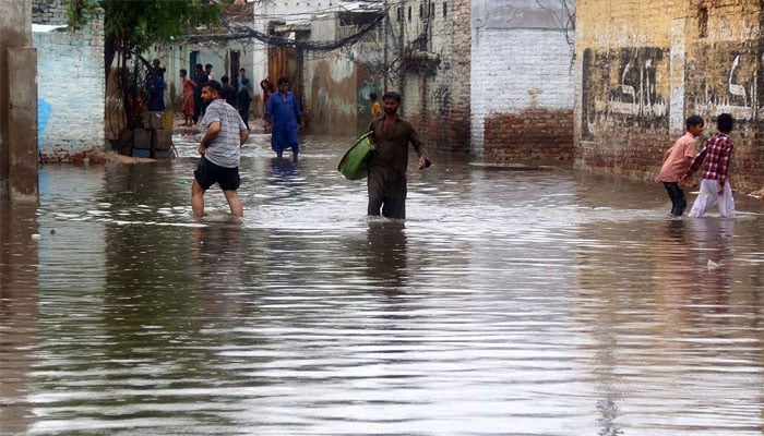 Commuters wade through a flooded road after heavy rainfall at Main Qasimabad road in the city.— Online/File