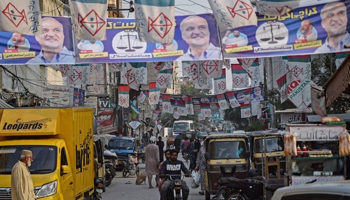 Commuters move past the election banners of Muttahida Qaumi Movement-Pakistan (MQM-P) and Jamaat-e-Islami (JI) parties hung over a street ahead of the upcoming general elections, in Karachi on January 24, 2024. — AFP