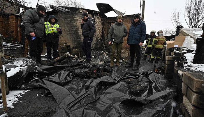 Some police members stand in front of bodies covered by plastic bags at the site of a Russian drone attack in Kharkiv on February 10, 2024. — AFP
