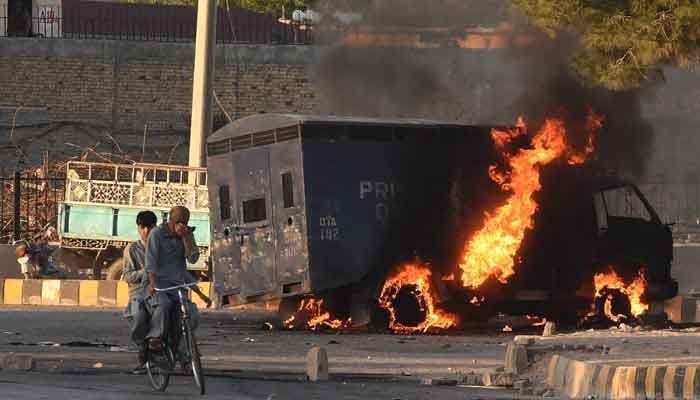 Men on a bike ride past a burning police vehicle during a protest by PTIs activists against the arrest of Imran Khan in Quetta on May 9, 2023. — AFP