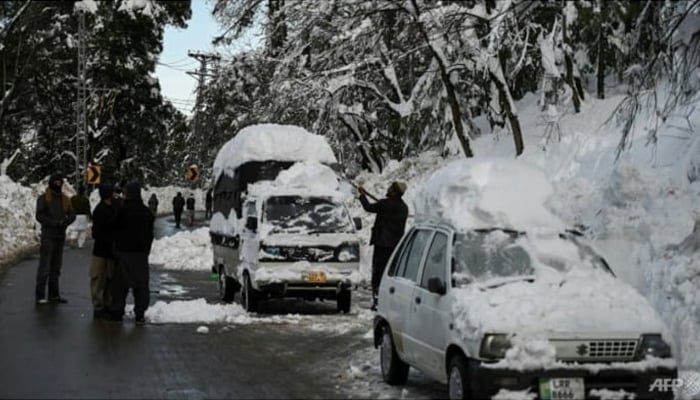 A man tries to clear snow off a vehicle on a road in Murree. — AFP/File
