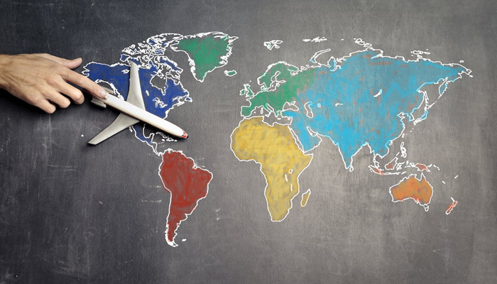 This image shows a person placing a dummy plane on a global map. — Pexels