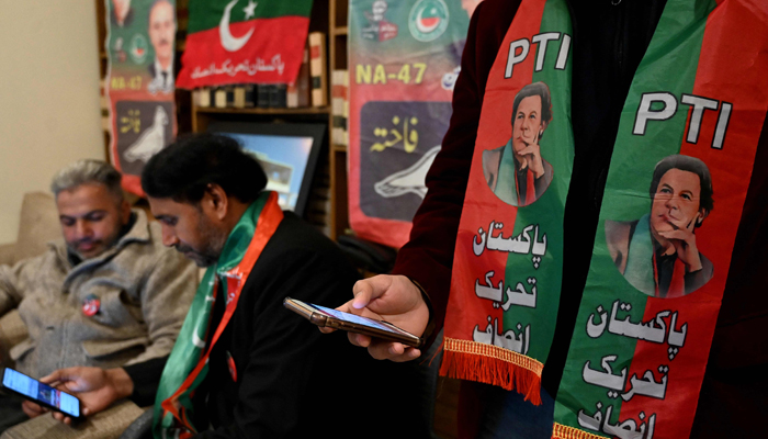 Pakistans former PM Imran Khans supporters wear scarves with prints of his PTI as they listen to a virtual election campaign on phones at a PTI office in Islamabad on February 3, 2024. — AFP
