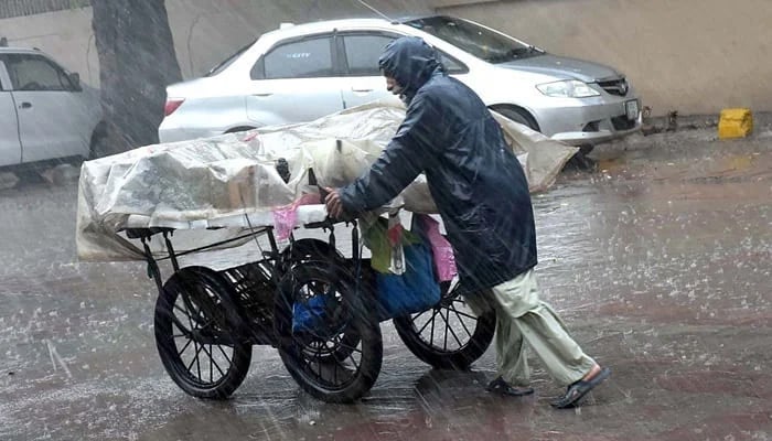 A street vendor pushing his handcart loaded with vegetables during heavy rain in Sialkot. — APP/File