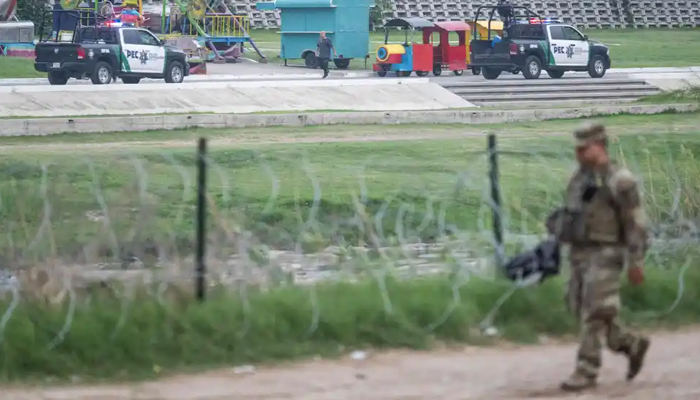 Members of the Mexican police patrol their side of the border, as a member of the US military walks past a barbed wire fence in Eagle Pass, Texas, on May 10, 2023. — AFP