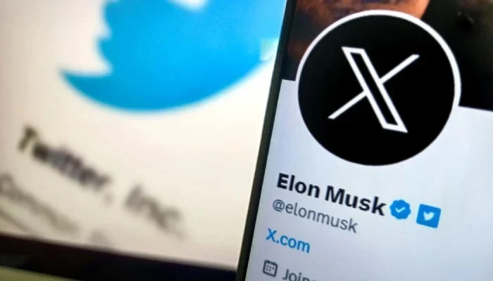 A phone screen showing Twitters new logo on Elon Musks Twitter handle with the older Twitter logo in the background. — AFP/File