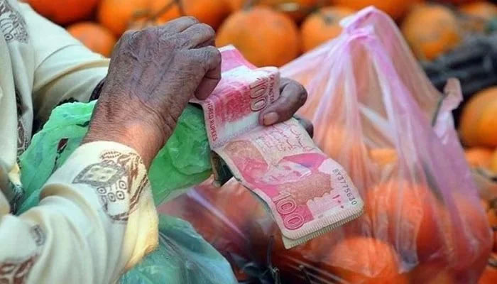 Man counts Pakistani currency notes next to a bag of groceries kept on a cart. — AFP/File