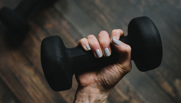 The representational image shows a woman holds a dumbbell for workout. — Unsplash