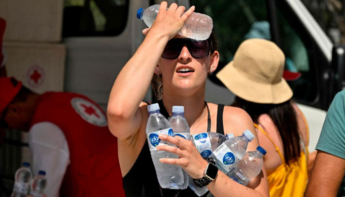 A woman cools off with cold bottles of water, distributed by the hellenic red cross organisation near the entrance of the Acropolis archaeological site in Athens. — AFP/File