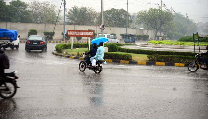 Commuters make their way to a road amid rain showers, near Governor House in Karachi on, March 1, 2024. — PPI