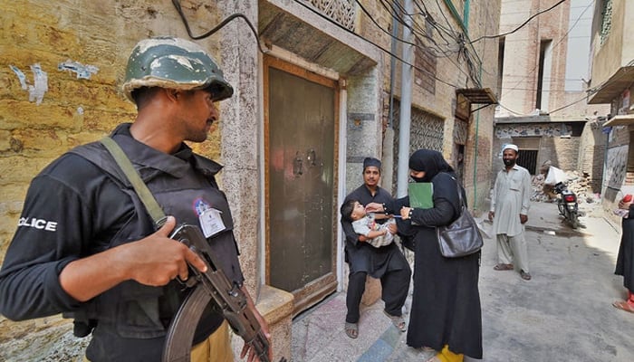 A policeman stands guard as a health worker administers polio drops to a child in Peshawar. — AFP/File