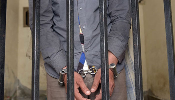 A representational image of a person handcuffed behind bars. — AFP/File
