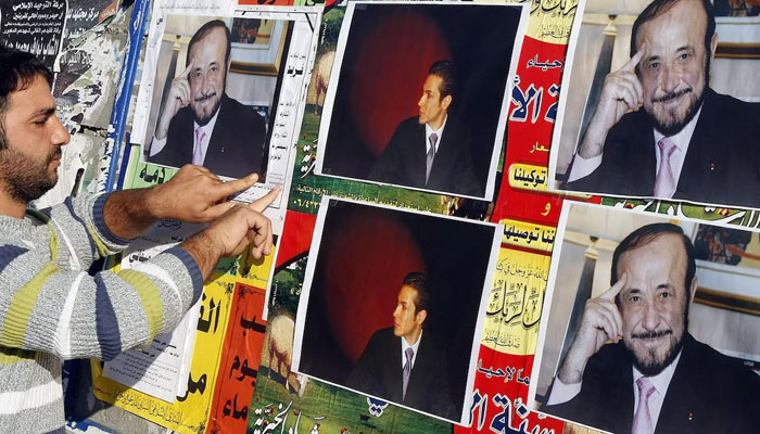 A member of the Alawite community pastes on a wall, pictures of Syrian opposition leader Rifaat al-Assad (R) and his son Ribal in the northern Lebanese city of Tripoli. — AFP/File