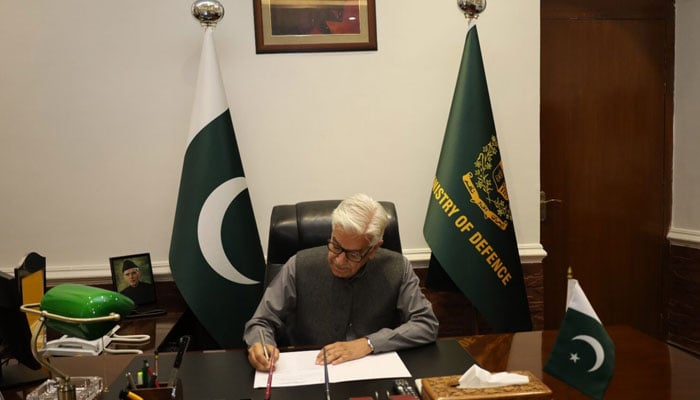 Minister of Defence Khawaja Asif can be seen while signing a document. — APP/File