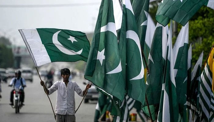 A vendor holds a Pakistani flag as he waits for customers beside his stall alongside a street in Islamabad. — AFP/File
