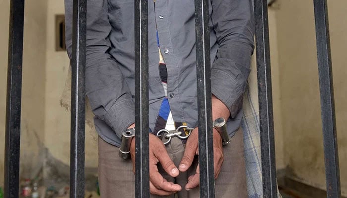 A handcuffed person can be seen behind bars in this image. — AFP/File