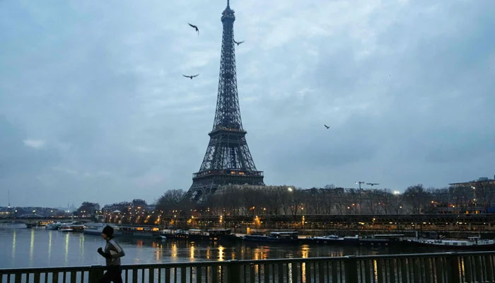 A resident runs on the snow-covered bridge of Grenelle in Paris, with the Eiffel Tower seen in the background, on January 18, 2024. — AFP