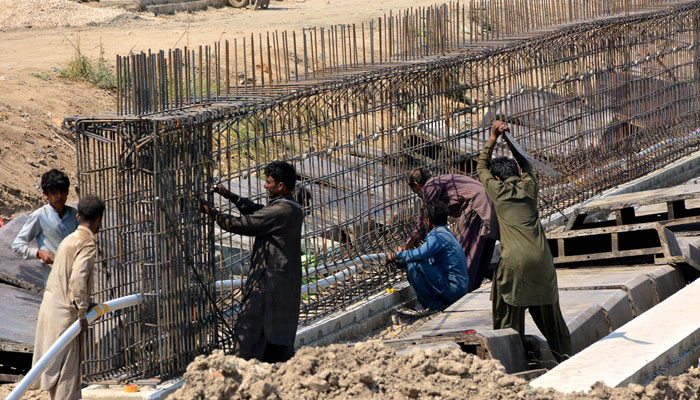 Labourers seen busy in construction work of wall of a water canal in Hyderabad city on March 18, 2024. — APP