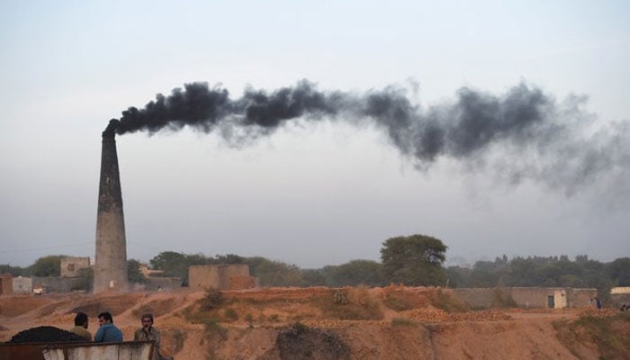 Smoke billows from a chimney as Pakistani labourers rest beside a brick kiln on the outskirts of Islamabad. — AFP/File
