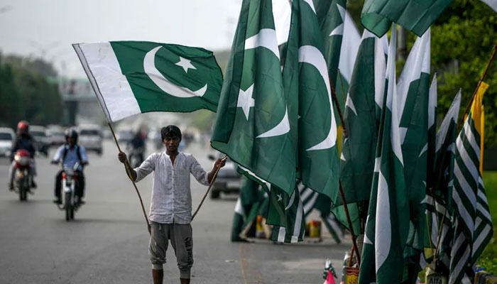 A vendor holds a Pakistani flag as he waits for customers beside his stall alongside a street in Islamabad. — AFP/File
