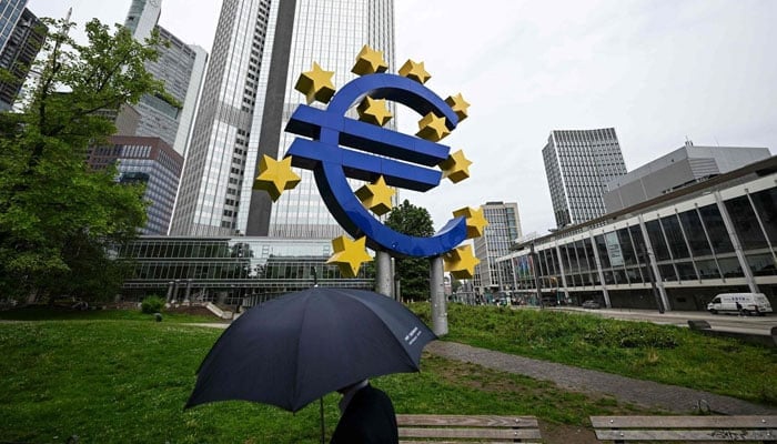 A man with an umbrella walks past the euro currency sign in front of the former European Central Bank (ECB) building, Frankfurt am Main, Germany, July 27, 2023. — AFP