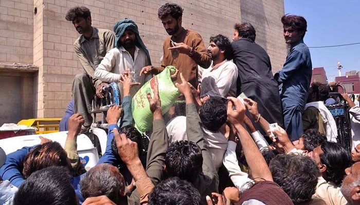 People attempt to get of hold of ration bags during distribution of ration bags as part of Ramazan package. — APP/File