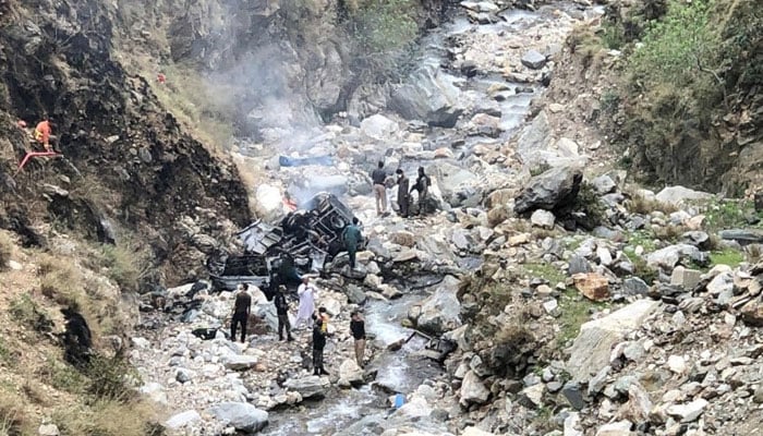 Security officials inspect the wreckage of a vehicle that plunged into a deep ravine after a suicide attack near Besham city in the Shangla district of KP on March 26, 2024. — AFP