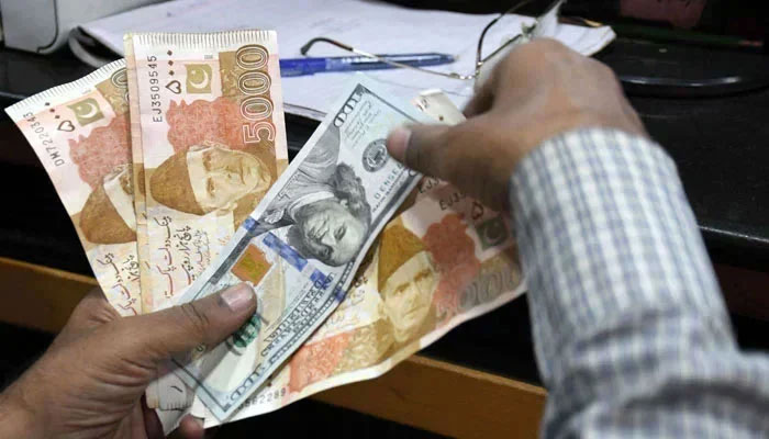 A money changer is seen holding currency notes of Pakistan and US dollars. — APP/File