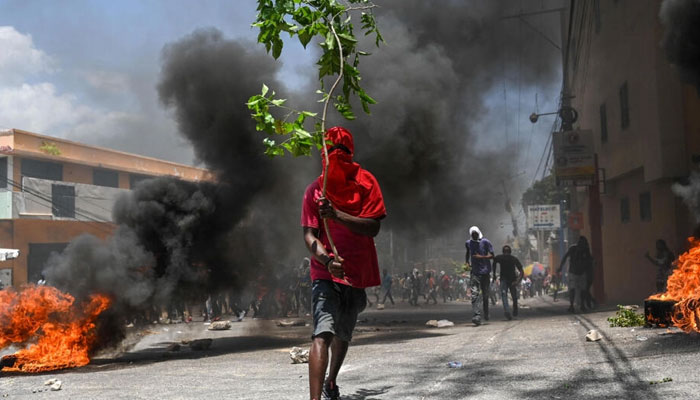 A man holds a tree branch and marches by burning tires during a protest against insecurity, on August 7, 2023, near the prime ministers official house in Port-au-Prince, Haiti. — AFP