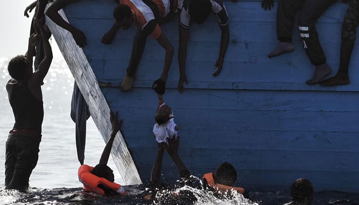 Migrants try to pull a child out of the water as they wait to be rescued 12 nautical miles north of Libya. — AFP/File
