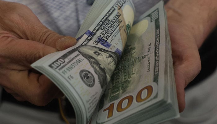 A teller flicks through a bundle of US dollar bills at an exchange office in Ankara on July 20, 2023. — AFP
