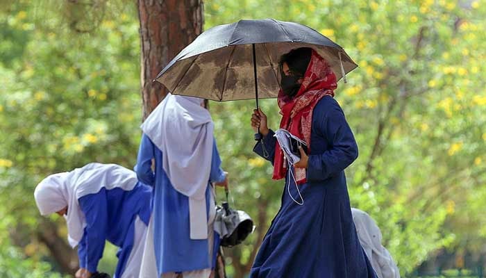 A girl walks under the cover of an umbrella to protect herself from direct sunlight during hot weather. — APP/File