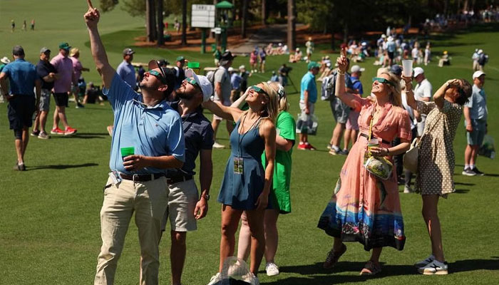 Patrons use glasses to view the eclipse during a practice round prior to the 2024 Masters. — AFP/File