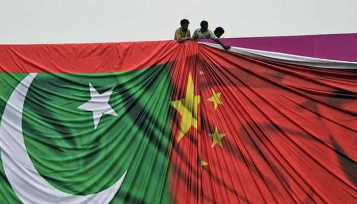 Workers put up a banner featuring flags of Pakistan and China at an event. — AFP/File