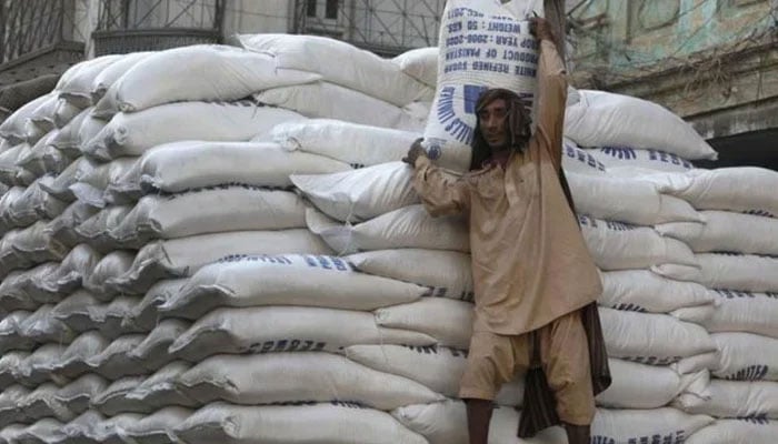A labour is pictured carrying a sugar bag with a large number of sugar bags stacked behind him. — AFP/File