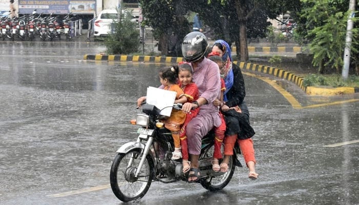 A family pictured while travelling on a motorcycle during rainfall in Lahore. — Online/File