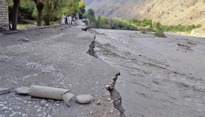 People stand alongside a washed away road in KP. — APP/File