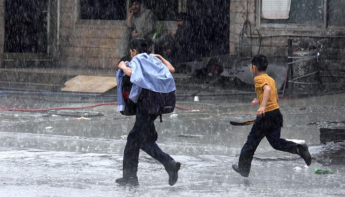 Chilren walk during rain in Rawalpindi on April 15, 2024. — APP