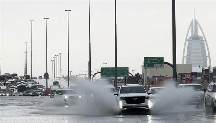 An SUV splashes through stagnant water on a road with the Burj Al Arab hotel seen in the background in Dubai, UAE on April 16, 2024.  — AFP