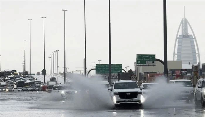An SUV splashes through stagnant water on a road with the Burj Al Arab hotel seen in the background in Dubai, UAE on April 16, 2024. — AFP
