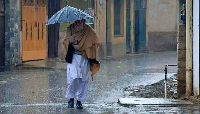 An old man covering himself with an umbrella during rain in Peshawar. — APP/File