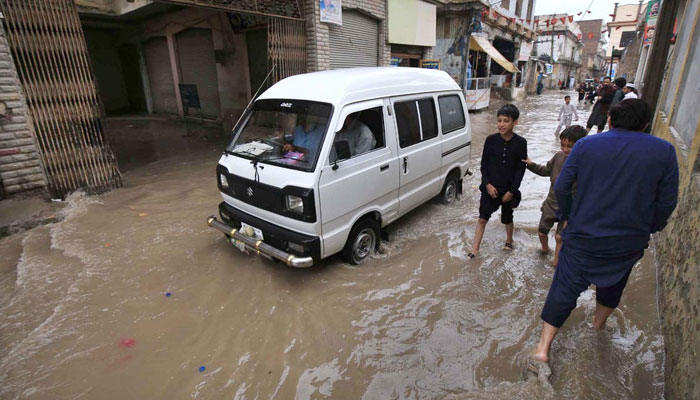 A vehicle and people passing through rainwater in the street after heavy rain in KP on April 19, 2024. — APP