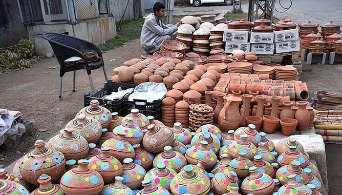 A vendor arranging and displaying the different kinds of clay pots to attract the customers at roadside setup. — APP File