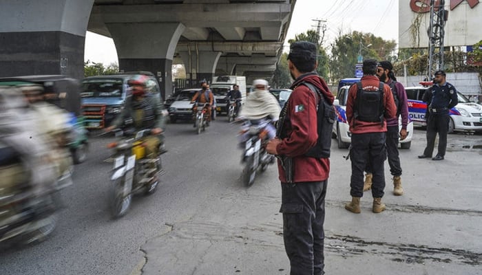 Policemen stand guard as traffic flows on a road in Peshawar. — AFP/File