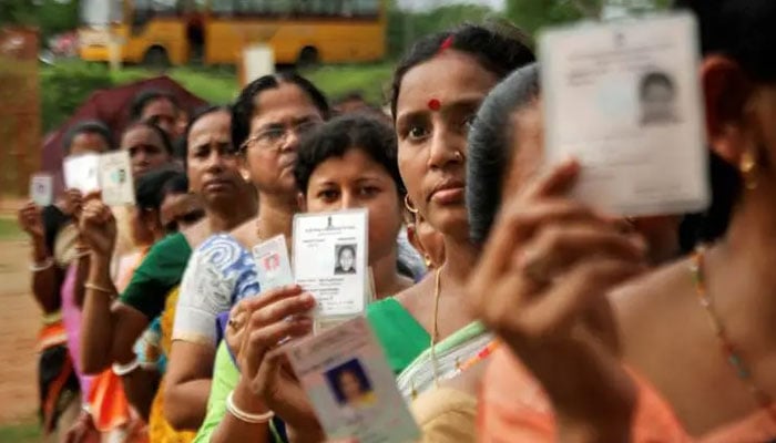 Women show their voter identity cards as they stand in a queue before casting their votes in Agartala. — PTI
