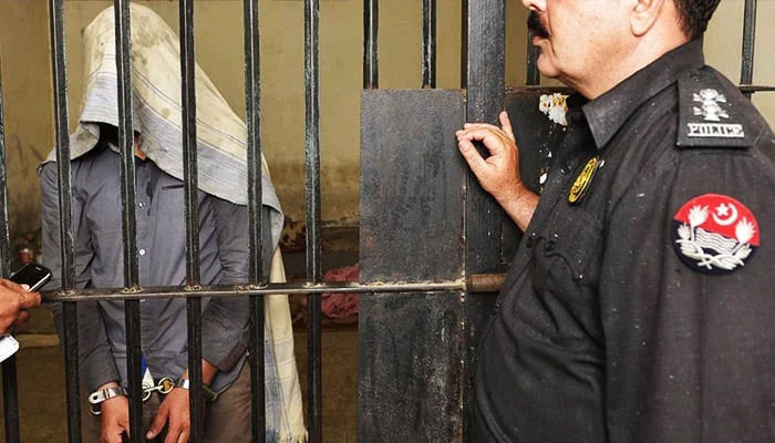 A handcuffed suspect stands behind the bars with a policeman standing outside the jail in this undated image. — AFP/File