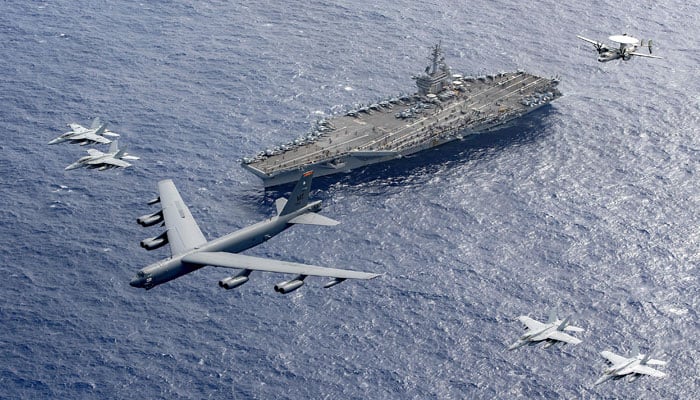 A US Air Force B-52 bomber flanked by F-18 fighter aircrafts fly over US Navys aircraft carrier USS Theodore Roosevelt. — X/@USNavy/File